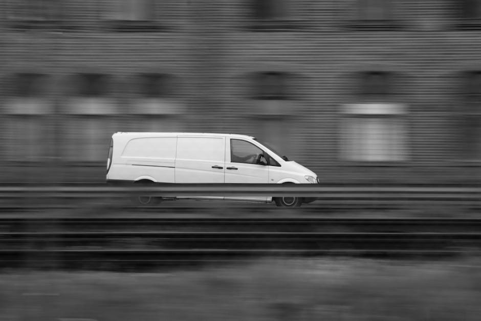 A white commercial van operated by Man with Van Edmonton is seen in motion on a multi-lane road, with a blurred background of a brick wall and street features indicative of an urban environment. The van is positioned centrally in the image, with its side doors visible, suggesting a home relocation or furniture transport process. The vehicle is equipped for removals services, suitable for loading household furniture, boxes, and packaging materials. The setting appears to be daytime, with natural lighting illuminating the vehicle, and the blurred motion implies high speed typical of fast removals or logistics operations. This image captures the essence of professional removals, emphasizing efficient vehicle use in the urban moving industry, aligning with the topics covered in Edmonton Green: Best Van Routes for Fast Removals, EDMONTON from [COMPANY_NAME].