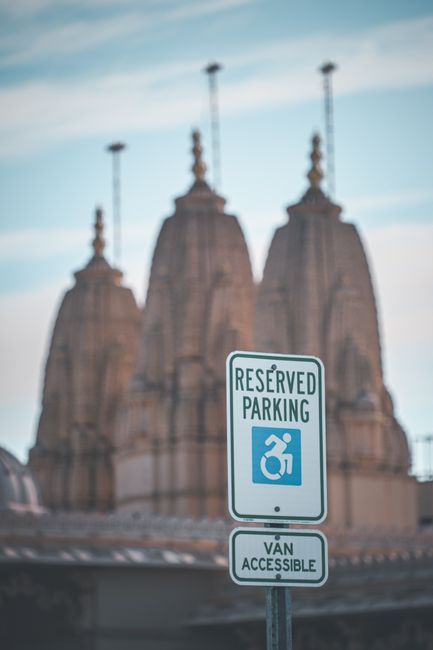 A close-up view of a reserved parking sign indicating van accessibility, mounted on a metal pole with a white background and green lettering that reads 'RESERVED PARKING' along with a wheelchair symbo